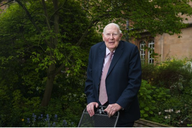Sir Roger Bannister, stood behind a chair in a college garden