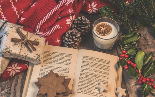 A book surrounded by Christmas gifts, pinecones and holly