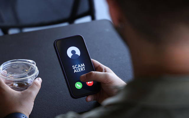 Person holds a mobile phone that says 'Scam Alert'