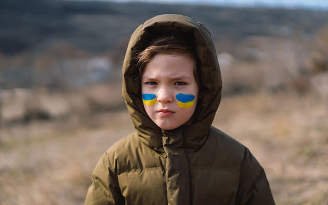 Young girl stares into the camera with Ukrainian flag colours painted on her cheeks