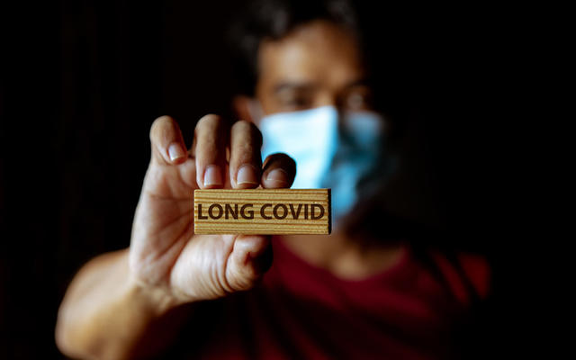 Masked man holds up piece of wood that says, 'Long Covid'