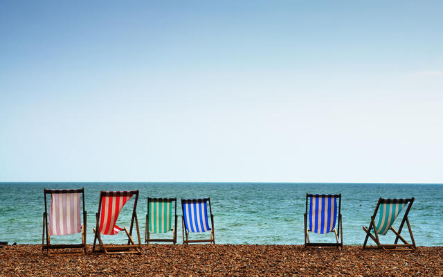 A row of six deckchairs on a shingle beach, pointing towards the sea