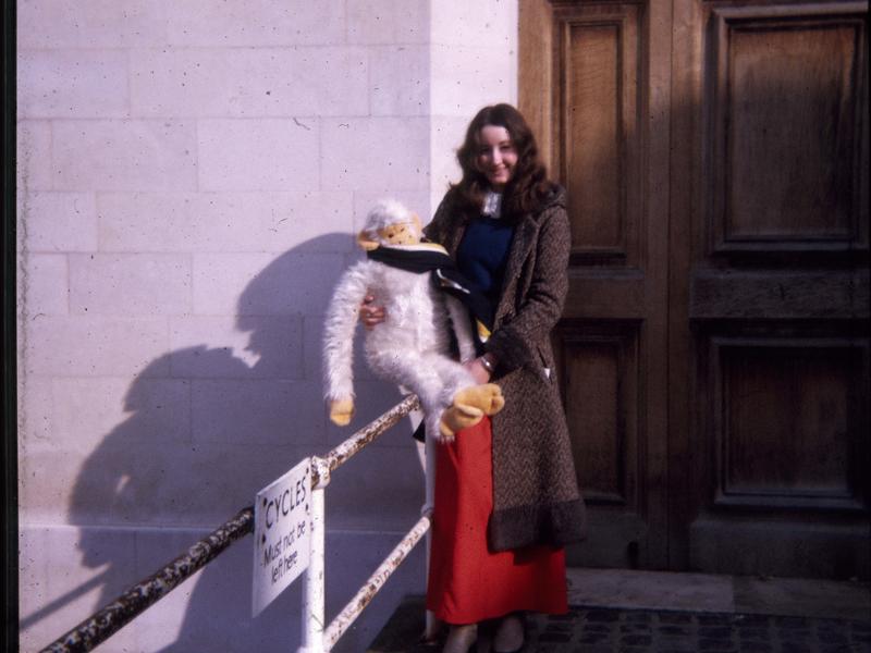Nicky Bull (nee Harper) on college steps, holding a large white, cuddly monkey which is wearing a college scarf