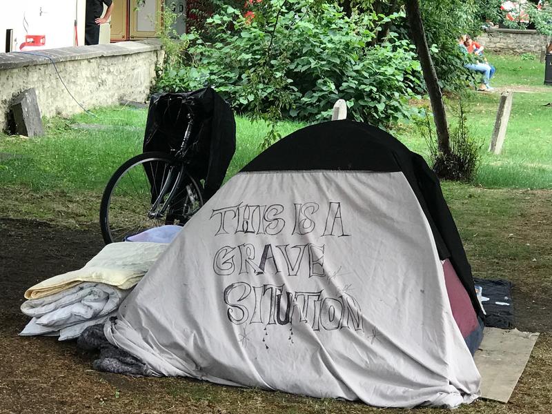 A tent in a graveyard - on the tent is written 'This is a grave situation'