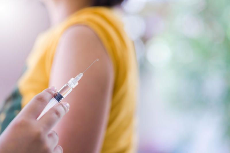 Syringe loaded up with flu vaccine in front of someone's arm Syringe loaded up with flu vaccine in front of someone's arm