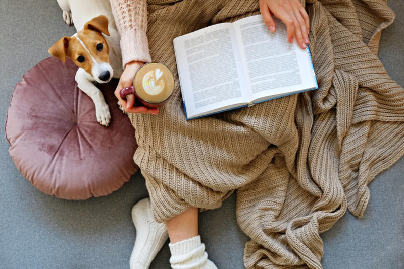 A person reading a book next to a small dog