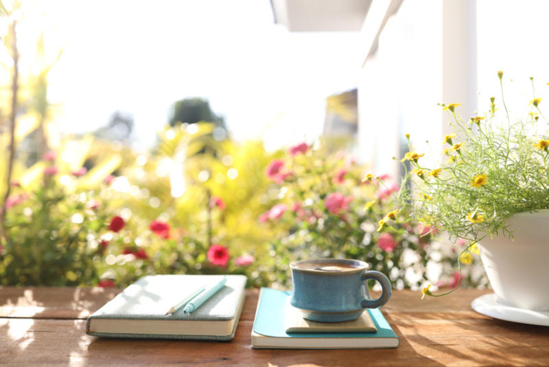 Two books and a cup of coffee amid sunshine and flowers