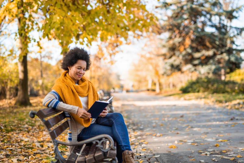A woman reads a book on a park bench, in autumn