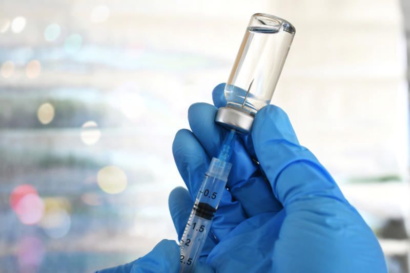 Blue-gloved hands hold up a vial of vaccine in a laboratory setting