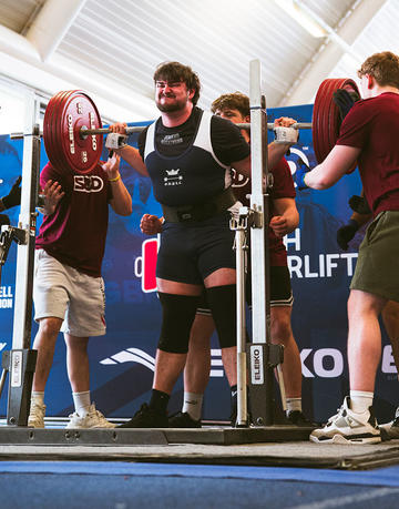 Will James lifting weights at the BUCS Powerlifting Championships, surrounded by people supporting him